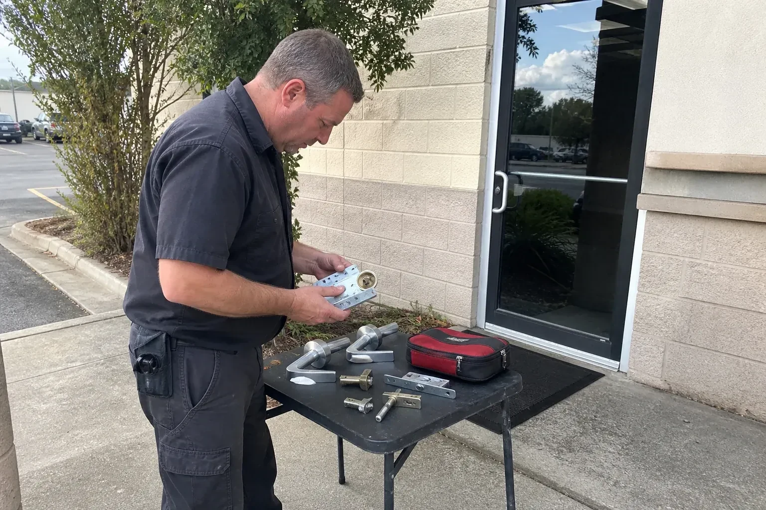 Technician examining detached commercial lock hardware on a table outside a shop entrance. — Business Lockout Service, Innisfil