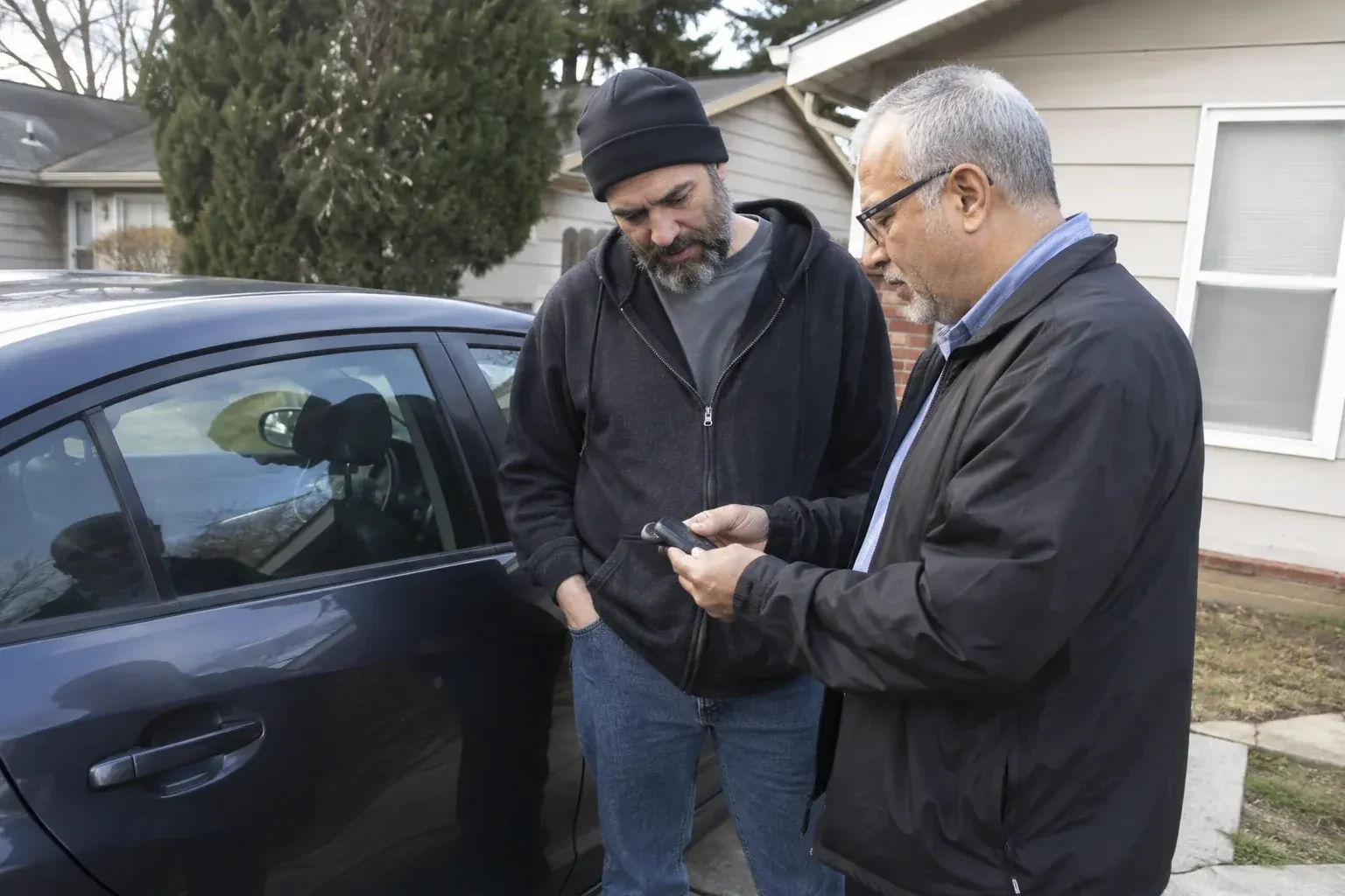 Two adults discussing a key fob beside a parked car. — Car Lockout Service, Innisfil