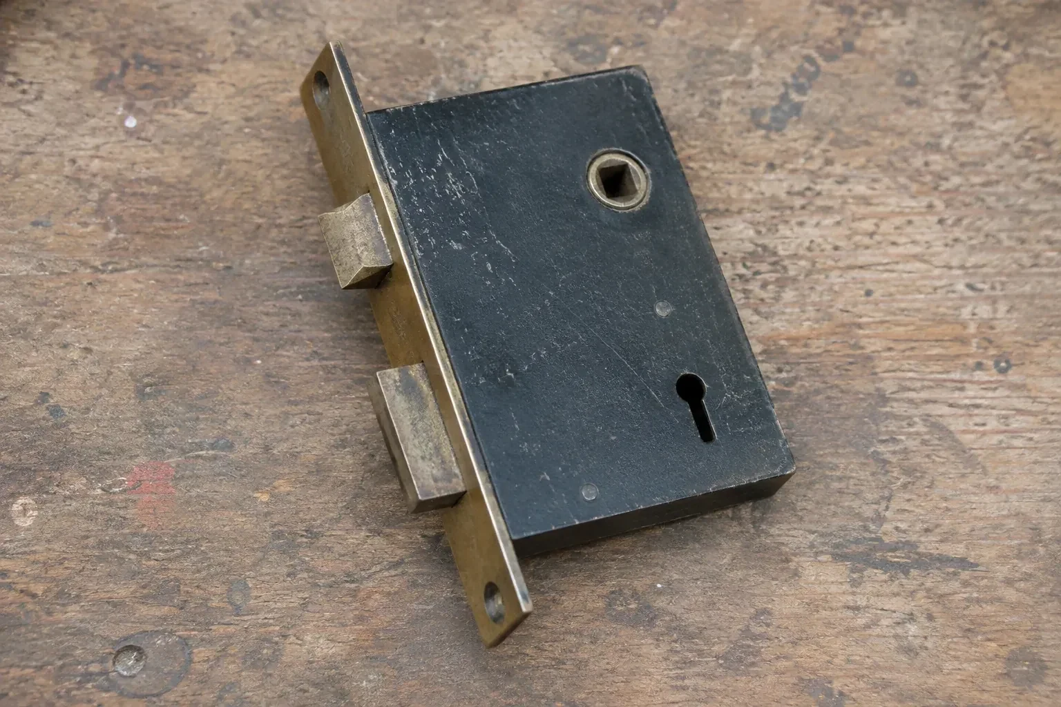 Closed mortise lock case with spindle opening, keyhole, latch and deadbolt on a wooden workbench. — Vintage Mortise Lock Service, Bear Point