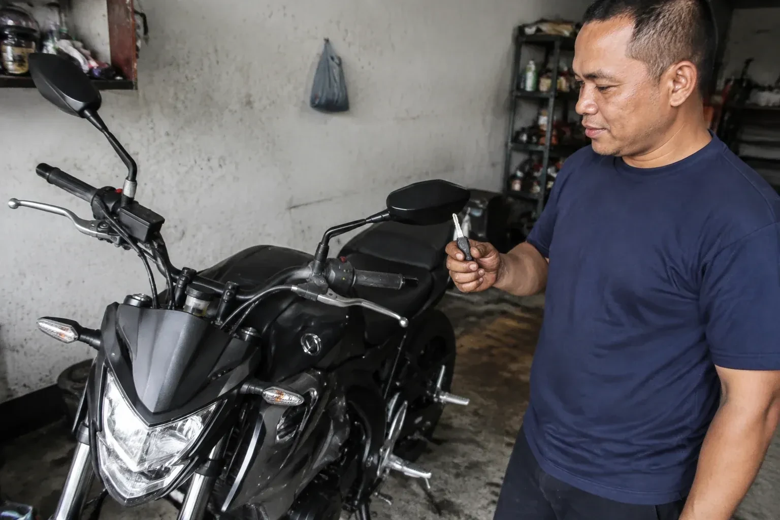 Person holding a key beside a black motorcycle in a garage. — Motorcycle & Scooter Keys, Innisfil